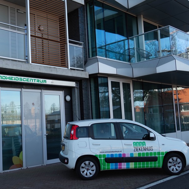 Voorzijde gebouw bloedafnamelocatie Gezondheidscentrum Hartje Eindhoven. Met geparkeerde auto met logo Anna Ziekenhuis. Bij het Anna Ziekenhuis kun je op meerdere locaties in de regio bloed laten afnemen en lichaamsmateriaal zoals urine en ontlasting inleveren.