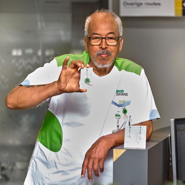 Foto van Fred Apon in dienstkleding waar hij trots een klavertje vier laat zien Patiëntenbegeleider Fred Apon geeft patiënten die het moeilijk hebben een klavertje vier mee