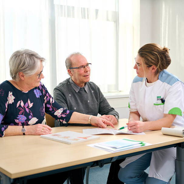 Patiënt en dokter zitten naast elkaar aan tafel, terwijl ze spreken over een boek dat voor hen ligt Urologie klachten aan urinewegen
