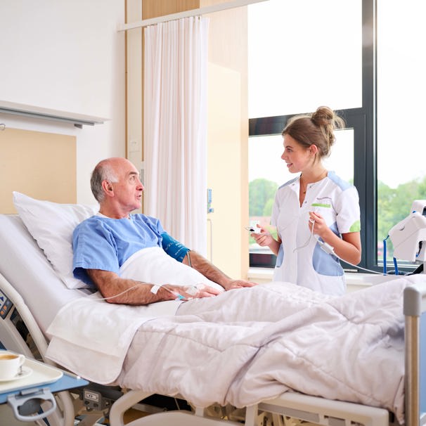 Patiënt ligt in ziekenhuisbed, zorgverlener staat naast hem met apparaat in haar handen De Acute Opname Afdeling (AOA) is voor patiënten die ongepland met spoed moeten worden opgenomen