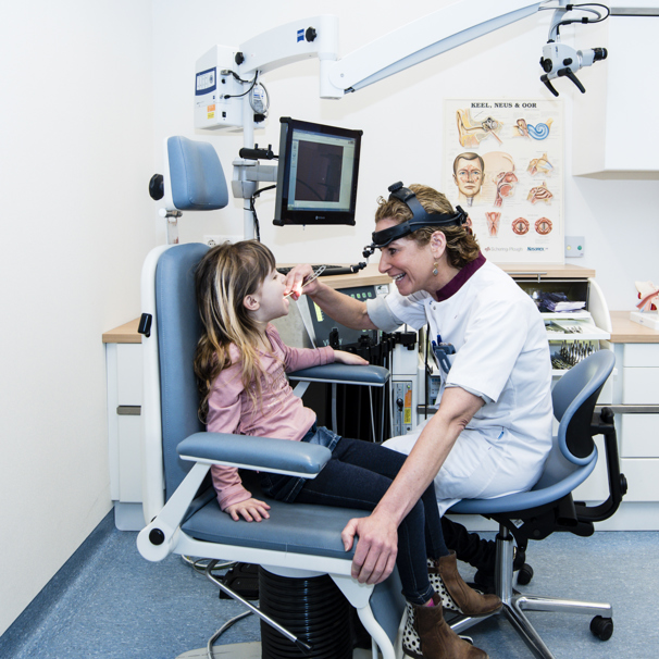 Kind zit in stoel, naast haar zit de kno-arts die met een medisch hulpmiddel in haar keel kijkt Keel-neus-oorheelkunde (KNO) voor volwassenen en kinderen