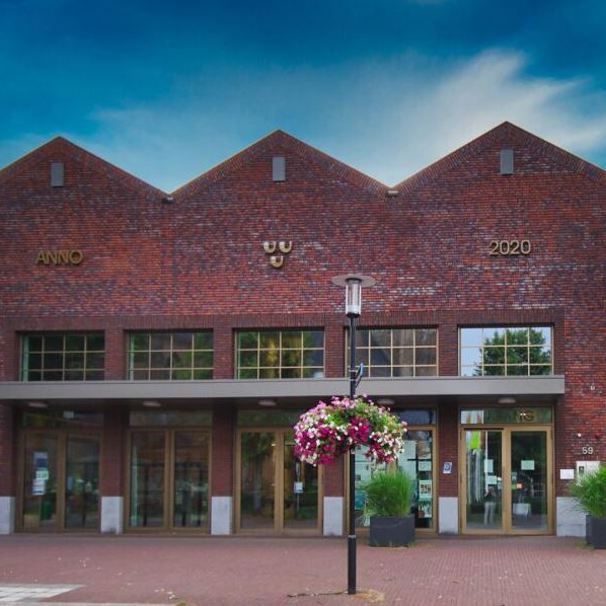 Voorzijde gebouw bloedafnamelocatie Dorpshuis De Schammert in Leende. Met geparkeerde auto met logo Anna Ziekenhuis. Bij het Anna Ziekenhuis kun je op meerdere locaties in de regio bloed laten afnemen en lichaamsmateriaal zoals urine en ontlasting inleveren.