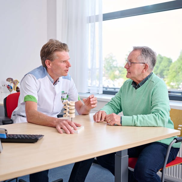 Patiënt zit op stoel aan tafel, dokter zit naast hem op stoel met medisch instrument in zijn hand. Ze zijn in gesprek Interne geneeskunde richt zich op onderzoek en behandeling van ziekten van de inwendige organen