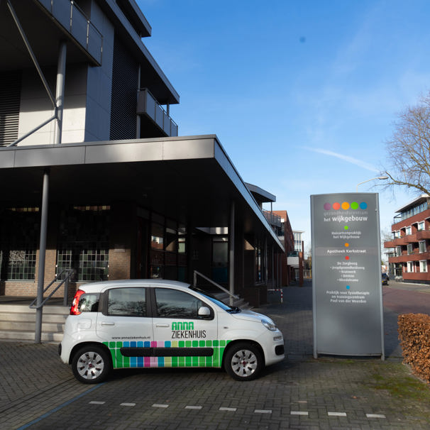 Voorzijde gebouw bloedafnamelocatie Wijkgebouw in Someren. Met geparkeerde auto met logo Anna Ziekenhuis. Bij het Anna Ziekenhuis kun je op meerdere locaties in de regio bloed laten afnemen en lichaamsmateriaal zoals urine en ontlasting inleveren.