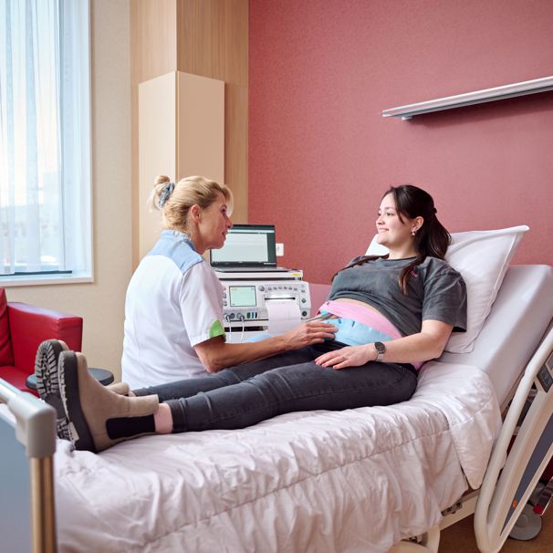 Zwangere vrouw ligt op ziekenhuisbed met band om haar buik, naast het bed zit een zorgverlener met een medisch apparaat In het geboortecentrum krijgen jij en jouw baby optimale zorg tijdens en na de bevalling