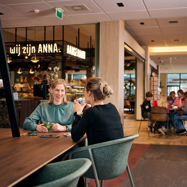 Twee personen drinken kopje koffie in de koffiecorner in de centrale hal In onze koffiecorner in de centrale hal kun je terecht voor een kopje koffie, iets lekkers of een cadeautje