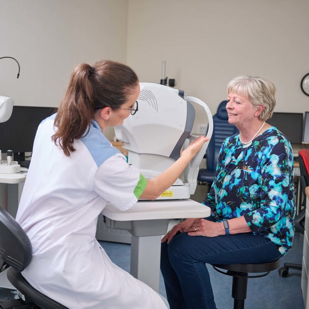 Patiënt zit op stoel voor apparaat om ogen te meten, dokter zit aan de andere kant van een apparaat en stelt deze in Oogheelkunde en oogmetingen