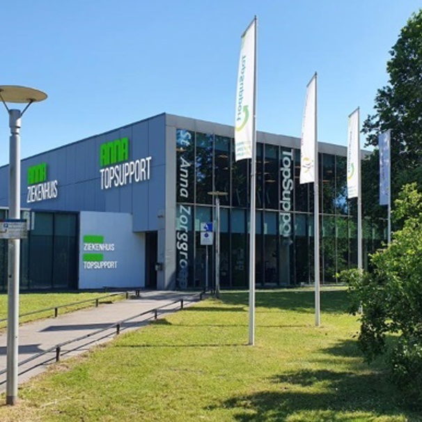 Voorzijde gebouw bloedafnamelocatie Anna Ziekenhuis in Eindhoven. Met geparkeerde auto met logo Anna Ziekenhuis. Bij het Anna Ziekenhuis kun je op meerdere locaties in de regio bloed laten afnemen en lichaamsmateriaal zoals urine en ontlasting inleveren.