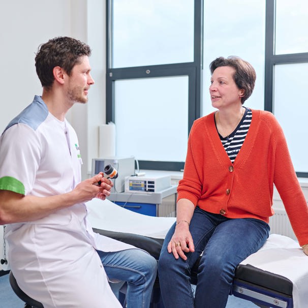 Patiënt zit op behandeltafel, dokter zit naast haar op een stoel. Ze zijn in gesprek met elkaar Dermatologie voor onderzoek, diagnose, voorlichting, advies en behandeling van huidklachten en huidproblemen