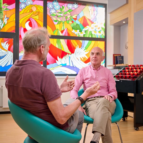 Patiënt zit in stoel en is in gesprek met geestelijk verzorger die tegenover hem zit Geestelijke verzorging voor een vertrouwelijk gesprek of steun na slecht nieuws